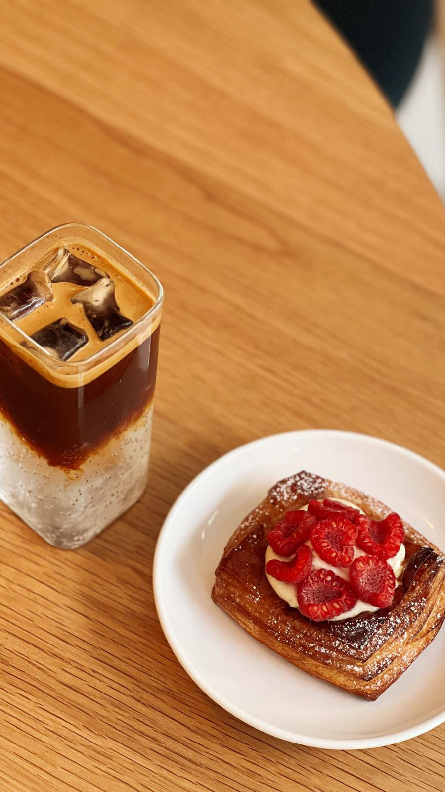 espresso tonic in tall glass with danish pastry with raspberries on a wooden tabel